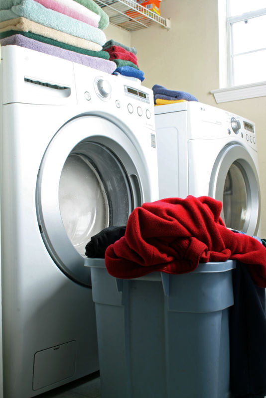 Laundry room with front load washer and dryer.  Towels and cloth folded on top with new load going into washer.  There is a red housecoat in top of the basket.