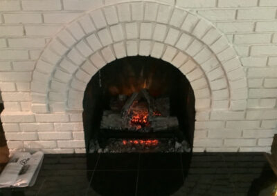 18 in electric gas logs installed in a white masonry fireplace that is arched.
