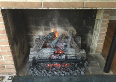 27 in electric logs in masonry brick fireplace with ash in the front of fire logs.