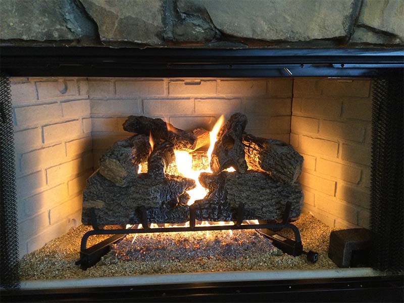 Gas Logs in New Factory Built Fireplace.  Flames are burning and the surround is made of large stones.