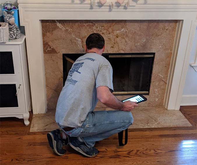 Technician performing an inspection of fireplace with marble surround and wood mantel.